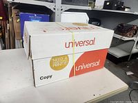 Box of Universal brand new white copy paper sealed with rubber bands on white table