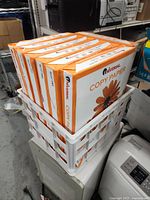 7 reams of Universal Copy Paper 11x17 size stacked in white plastic basket on a table in a storage area.