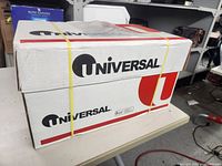 White cardboard box with Universal branding and red and black graphics, sealed with yellow rubber bands, containing the printer paper.