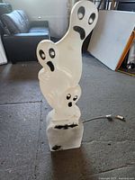 Front view of the three white plastic ghost figures stacked on a gravestone base with 'Happy Halloween' text and black painted features.