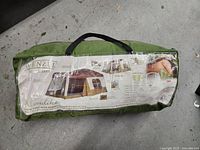 Photo of the packed tent in a green bag with printed label showing the tent design and branding.