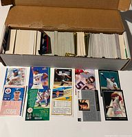 Box filled with trading cards, cards laid out showing front and flipped to show back. Cards include baseball and football players.