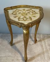 Front and angled view of antique Venetian side table showing ornate gold and white painted top with decorative floral design and three curved legs.