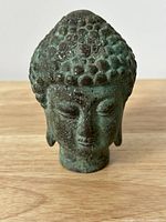 Front view of antique bronze Buddha head bust, showing detailed textured curls on hair, calm facial expression, and greenish patina.