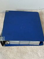 Closed blue three-ring binder with visible wear and damaged corners.