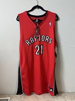 Front view of the red Toronto Raptors jersey with player number 21, Adidas branding, and hang tag.
