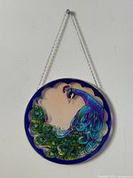 Front view of the round peacock art glass suncatcher hanging on the wall, showing full colorful design with cobalt blue border and suspension chain.