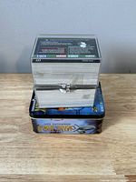 Large clear plastic box stacked with Star Trek trading cards, secured with clasp, placed on top of the metal collector tin