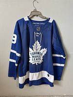 Front view of the Toronto Maple Leafs blue hockey jersey with white stripes and large maple leaf logo on chest. Lace-up neckline visible.