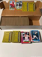 Photo showing a large stack of 1990 Topps Baseball cards in a cardboard box with some cards laid out in front including players Dave Bergman and Joe Girardi.