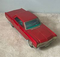 Three-quarter front view of red tin toy car showing body shape and paint