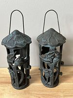 Front view of two vintage cast iron pagoda style lanterns with wire handles, showing detailed oxcidized patina and pagoda-shaped tops.