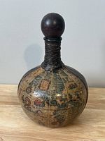 Front view of the round decanter showing old world map artwork and leather wrapped neck with wooden stopper.