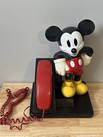 Front view of vintage Mickey Mouse telephone showing red handset and standing Mickey figure on black base.
