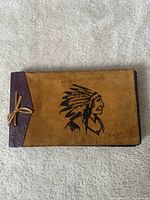 Album closed showing leather cover with Indigenous chief sketch and 'Photographs' text, tie closure on spine
