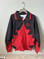 Front view showing black and red windbreaker with large red maple leaf design, front zipper, and Team Canada embroidered logo on chest.