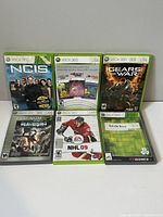 Front view of 6 Xbox 360 game cases showing titles NCIS, Xbox Live Arcade Games, Gears of War, Dead Rising Platinum Hits, NHL 09, and Score Classic Collection.