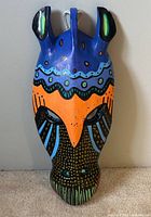 Front view of carved and painted zebra mask on carpeted floor.