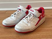 Side angle showing white leather Adidas x Marimekko sneakers with red accents, laces, velcro strap, and floral pattern