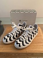 Front top-angle view of Adidas Stan Smith x Marimekko black and white striped sneakers with box behind.