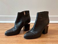 Front and side view of the pair of black leather ankle boots with block heels and visible rose gold toned hardware on heel edges.