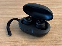 Black Bang & Olufsen Beoplay E8 wireless earbuds in open charging case showing earbuds in place and branded logo on earbud touch surface.