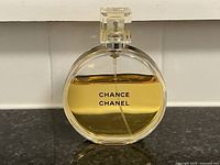 Round glass perfume bottle front view showing approximately over 3/4 full amber perfume liquid with 'CHANCE CHANEL' printed.