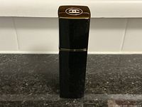 Front view of black rectangular Chanel perfume atomizer bottle with glossy finish and gold-toned top with white Chanel logo