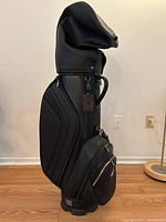 Side view of the black Genesis Motors Husky golf bag standing upright with travel cover on top, showcasing the smooth black material and handle.