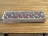 Boxed set of 4 aluminum napkin rings with wavy abstract shape, branded Iittala and marked Alvar Aalto Collection, clear lid showing the items inside.