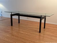 Full view showing clear glass top supported on black tubular steel base against wood floor.