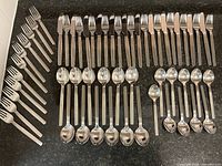 Full view of the flatware set laid out on a dark granite countertop showing all forks, knives, tablespoons, and teaspoons arranged orderly.