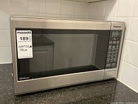 Front view of Panasonic stainless steel microwave on counter, showing whole unit with door and sticker displaying measurements.