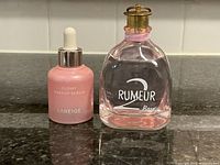 Front view of Rumeur 2 Rose perfume and Laneige Glowy Makeup Serum side by side on dark countertop.