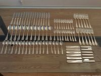 Full spread of the cutlery set showing knives, forks, spoons, dessert forks and spoons, and steak knives arranged on a wooden floor.