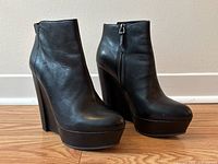 Pair of black leather ankle boots with high wedge heels shown from side angle, displaying smooth leather and zipper.