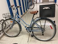 Side view of entire bicycle showing step-through frame, front wire basket, rear crate carrier and fenders