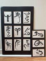 Large black framed artwork with nine ink calligraphy zodiac symbols arranged in a 3x3 grid with red seals.