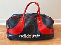Front view of vintage Adidas vinyl gym bag showing logo, red handles and corners on blue body.