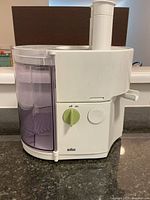 Front and side view of white Braun juicer showing translucent purple juice container and green rotary on/off knob