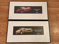 Photo showing two framed advertisement prints of the 2002 Ford Thunderbird from overhead. Prints feature red and gold Thunderbird cars with slogans on black backgrounds.