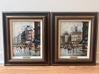 Frontal view of pair of framed oil paintings depicting rainy Paris street scenes, signed Celestin.