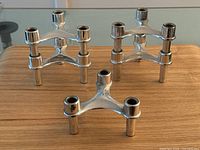 Five chrome finished plastic space age candlesticks arranged on a wooden surface, showing front and side views.