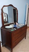 Full frontal view of antique wood dresser with mirror placed on top and various small items on glass surface.