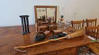 Photo showing antique iron pieces, wooden boxes, glass jars, rustic mirror, oil lamp, and broom on a wooden table.