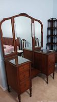 Front angled view of the antique vanity showing three large mirrors and three drawers on each side.