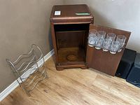 Wood bar cabinet interior view with eight etched glasses attached to open door and chrome wire wine rack beside cabinet.