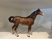 Side view of glossy brown ceramic horse figurine on white shelf