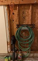 Photo of leaf blower, hoses coiled on black metal wall rack, orange extension cord hanging on wall hook, and miscellaneous small items on garage floor.