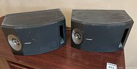 Pair of Bose 201V speakers side by side on a table showing front and side profile with visible dust and scuff marks on the surface.